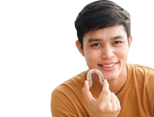 A boy is showing clear aligners and smiling after using Invisalign